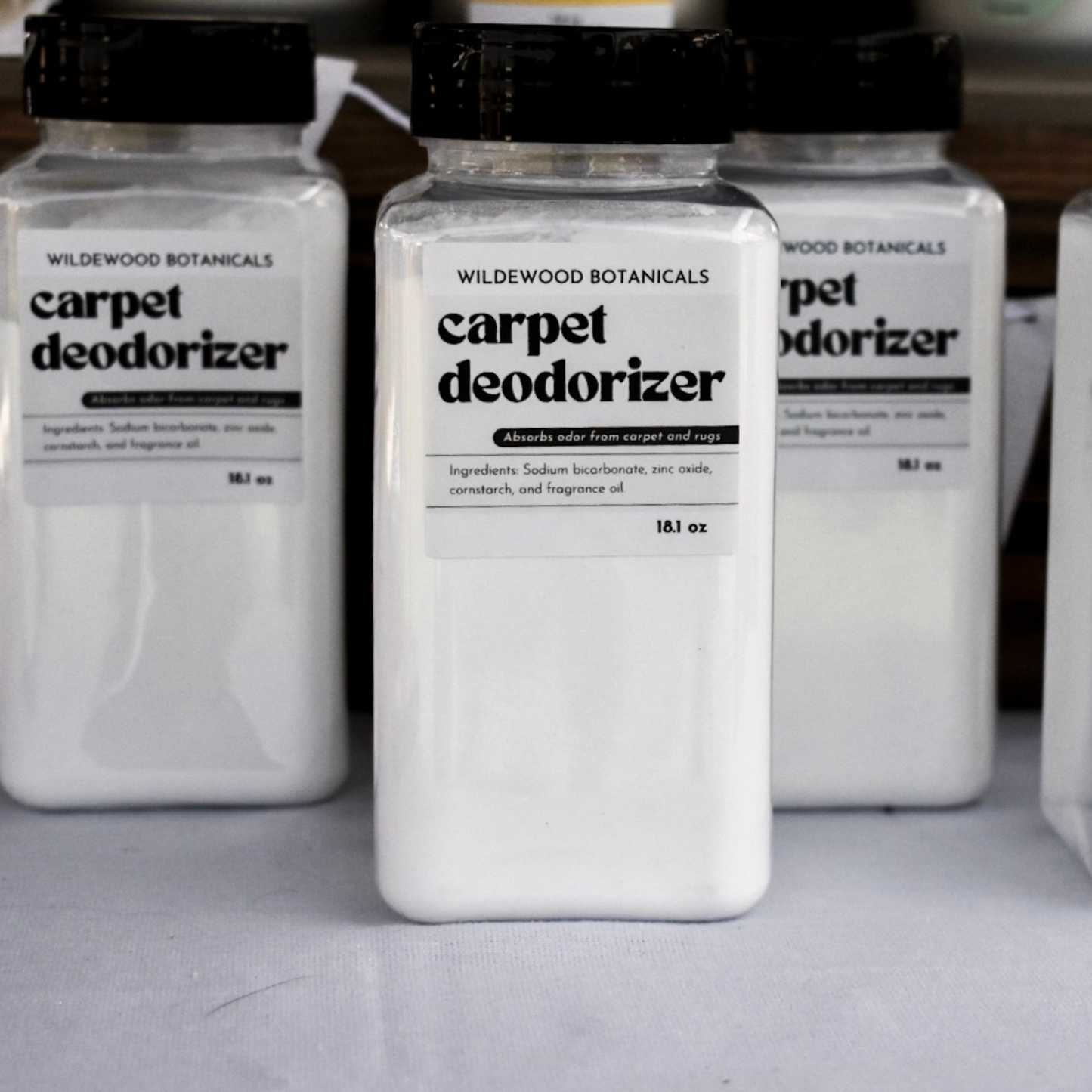 Three bottles of Wildewood Botanicals carpet deodorizer on a gray surface.