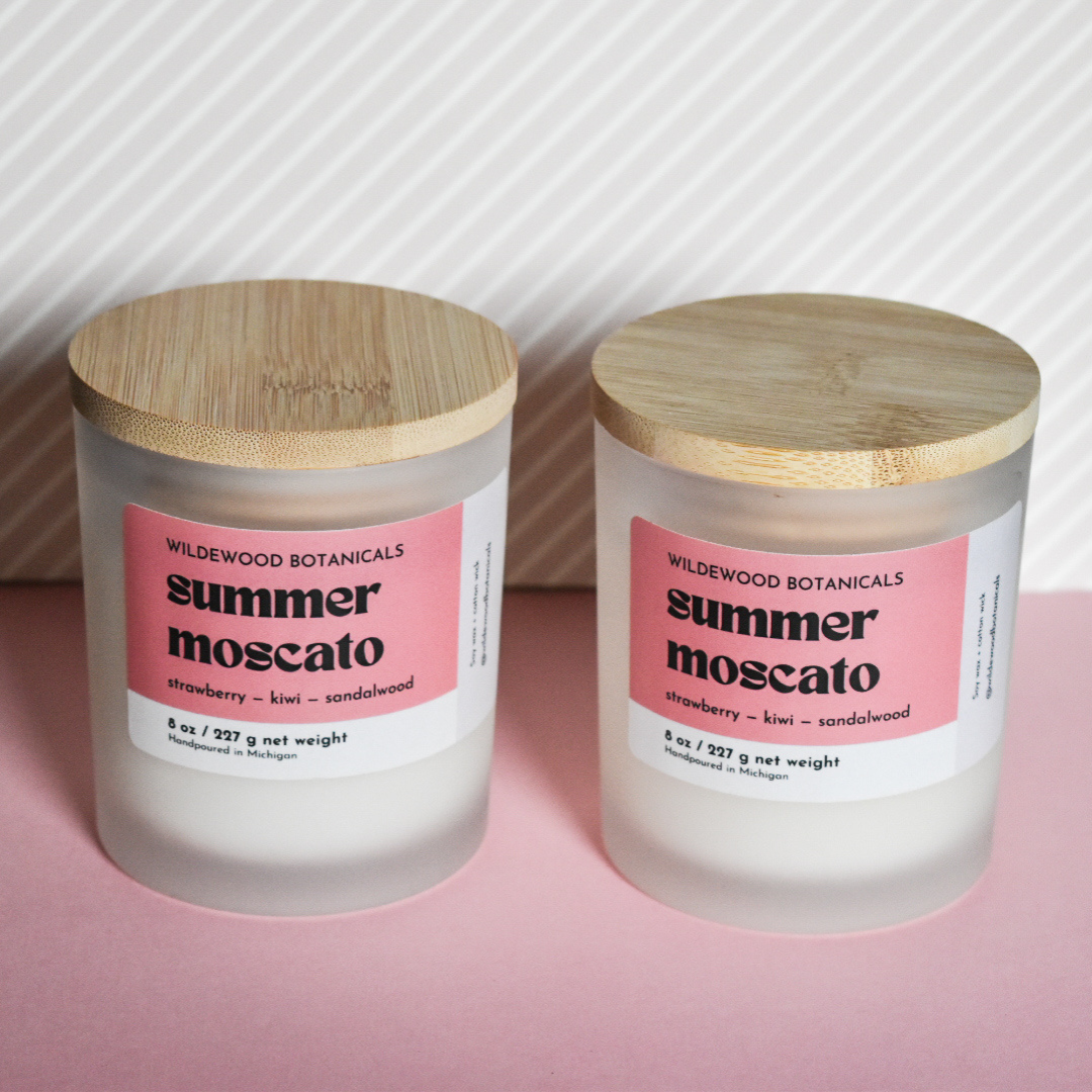 two regular size summer Moscato soy candles by wildewood botanicals on a pink and white striped background