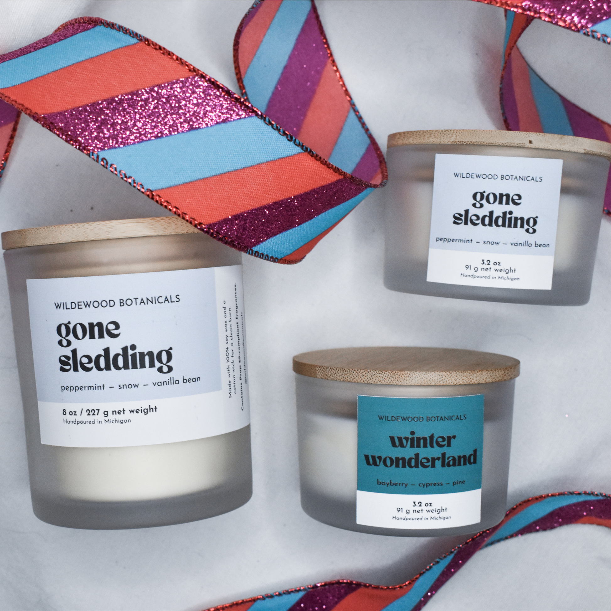 Three Gone Sledding soy candles with labels on a white background with colorful Christmas ribbons.