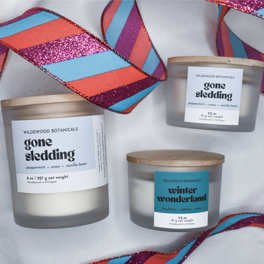Three Gone Sledding soy candles with labels on a white background with colorful Christmas ribbons.