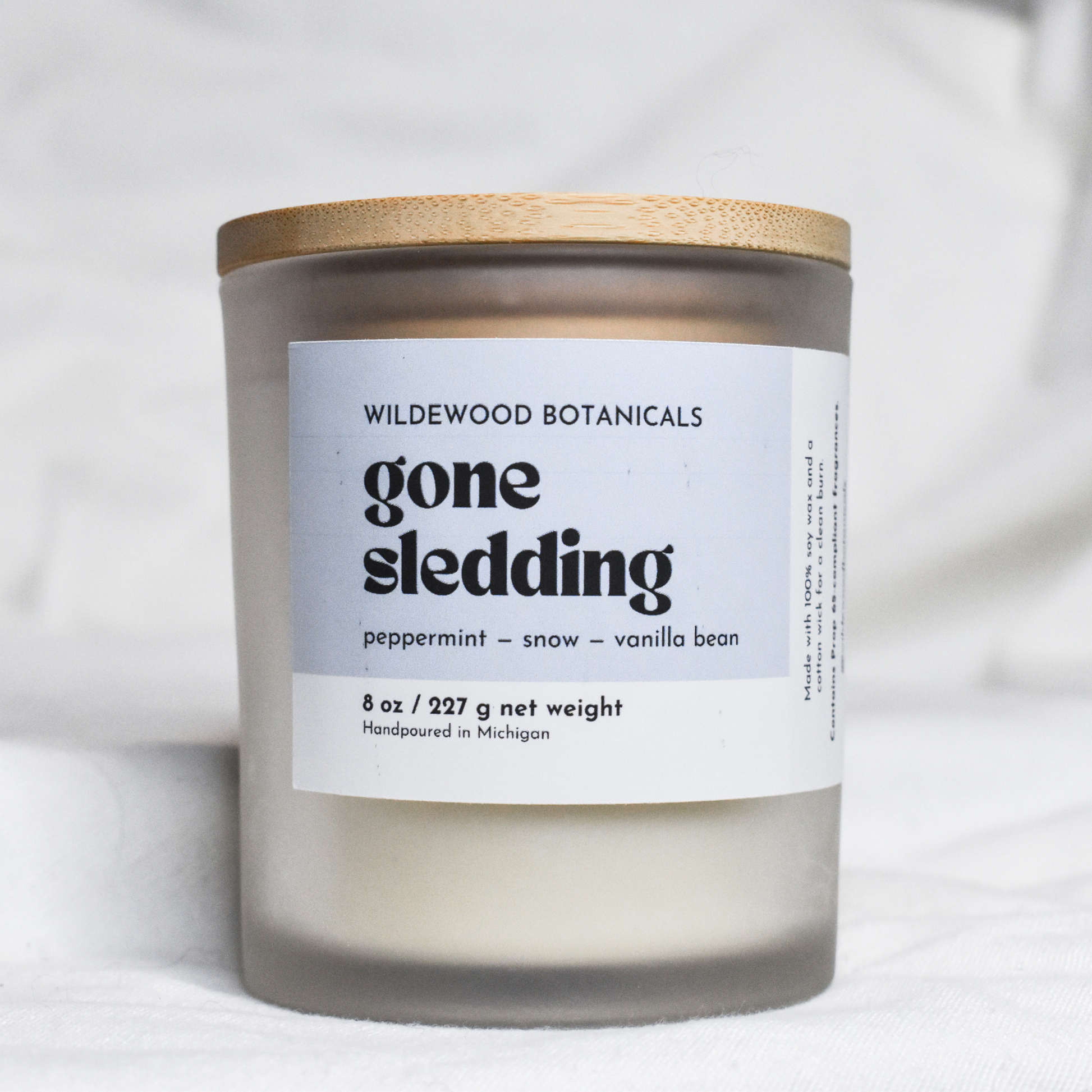 soy candle with a label reading 'gone sledding' by Wildewood Botanicals on a white background