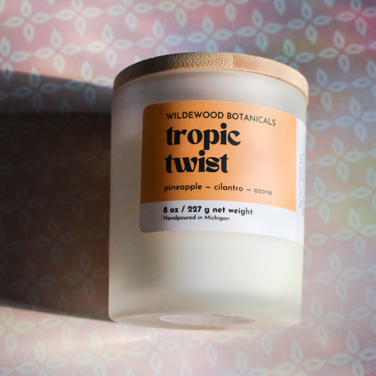 tropic twist soy candle in regular size, on a pink quatrefoil background with a rainbow sunbeam shining on it